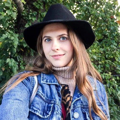 Kirby takes a selfie outside and is staring at the camera. She's wearing a jean jacket, sweater, and wide black hat.