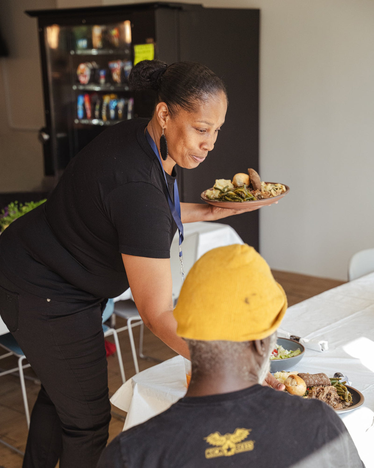 A woman sets a plate of food down on a table in front of a seated person