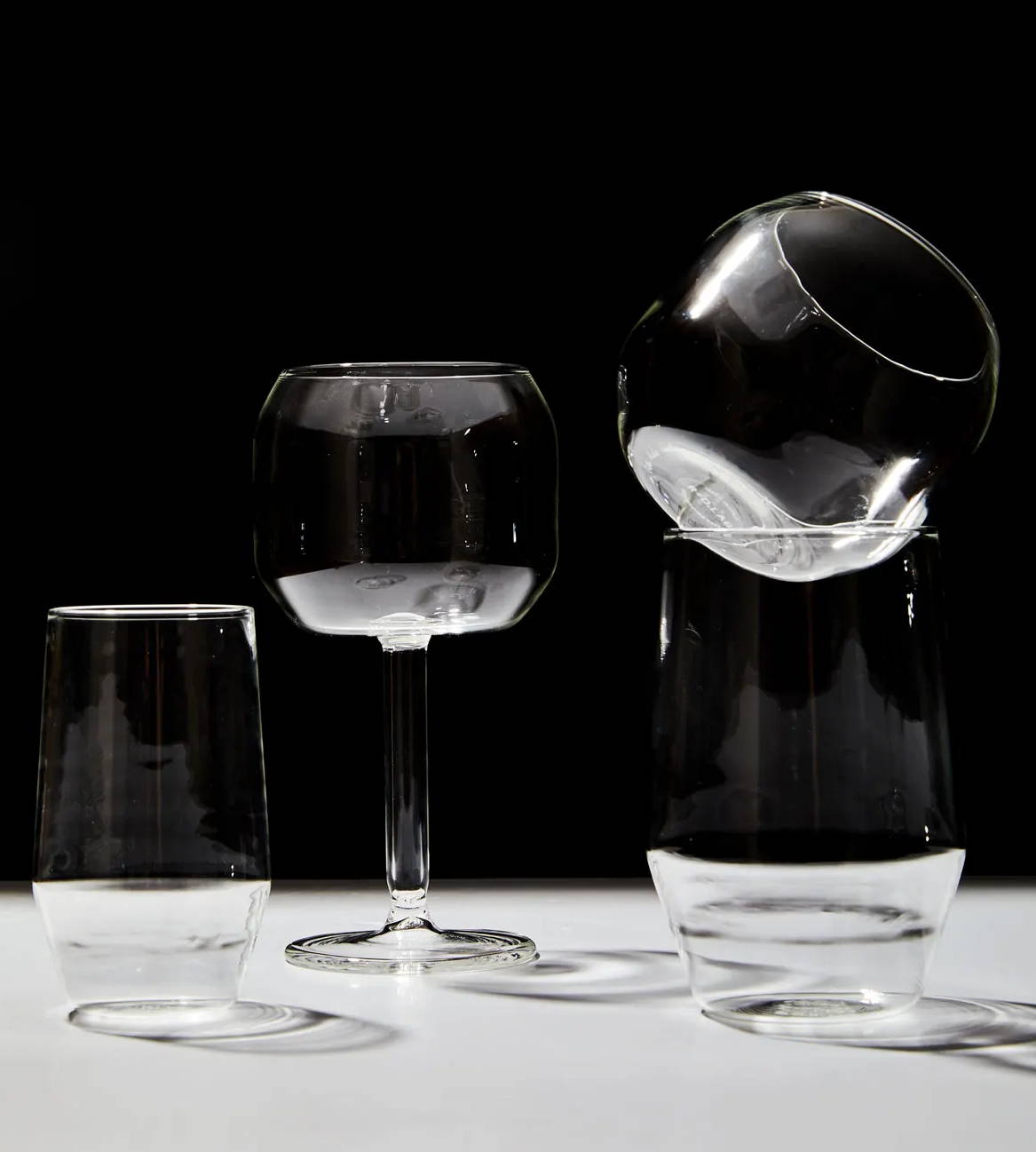 4 clear drinking glasses of various sophisticated shapes sit on a white surface with a black background.