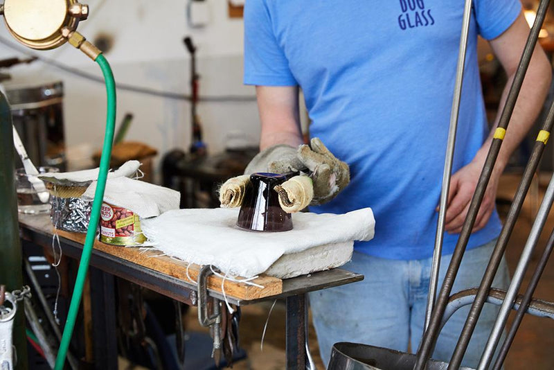 In a workshop setting, a person holds a glass upside down with special tools on a piece of fabric