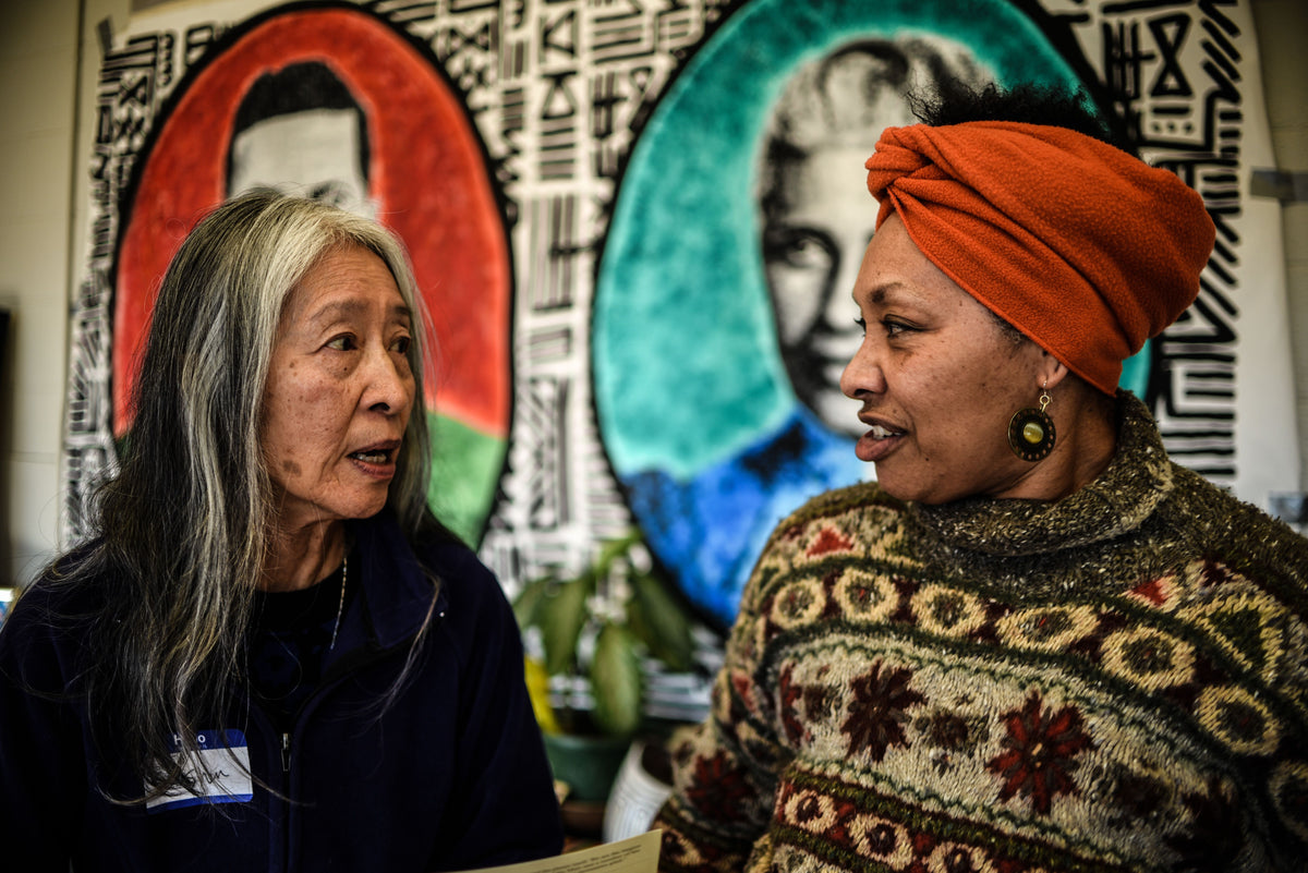 Two people are turned and looking at each other in the middle of a discussion in front of a vibrant mural