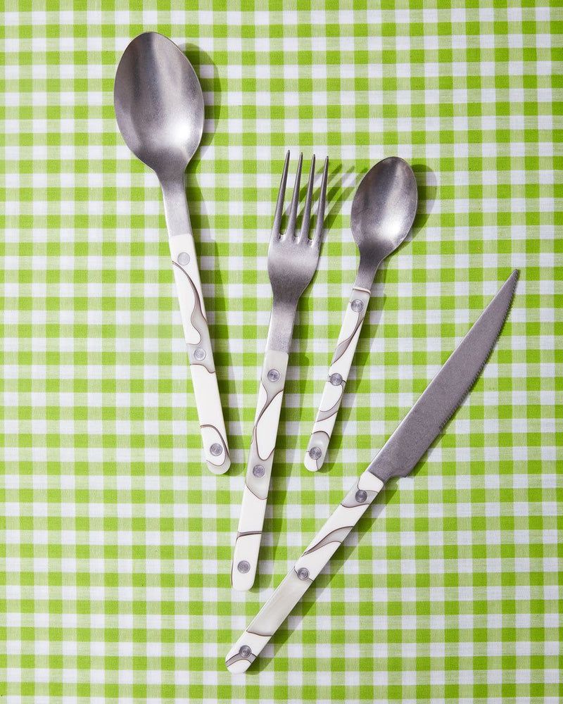 A soup spoon, dinner fork, teaspoon, and knife with white marbled handles sit against a lime gingham backdrop.