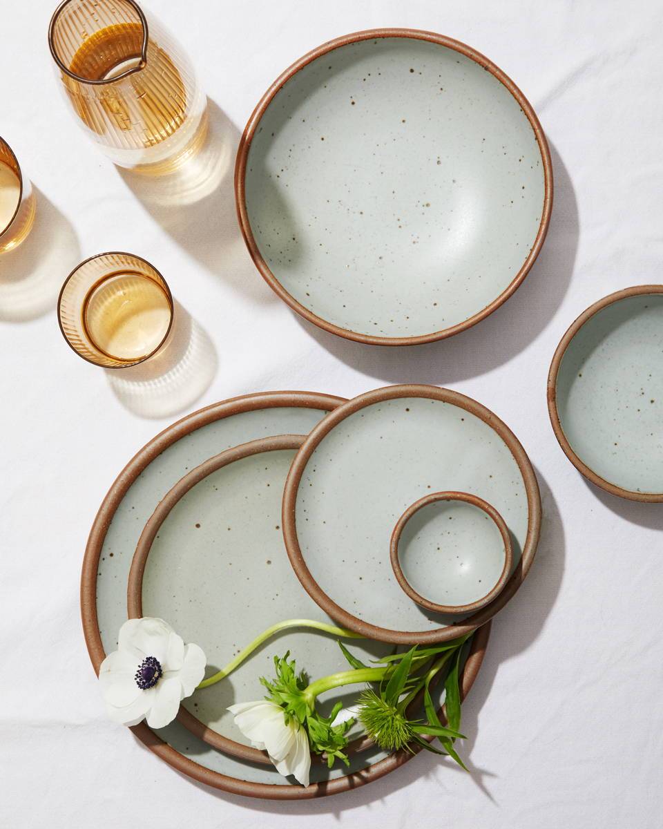 An artful arrangement of plates in various sizes in Soapstone, a light blue grey with some amber glasses and some anemones.