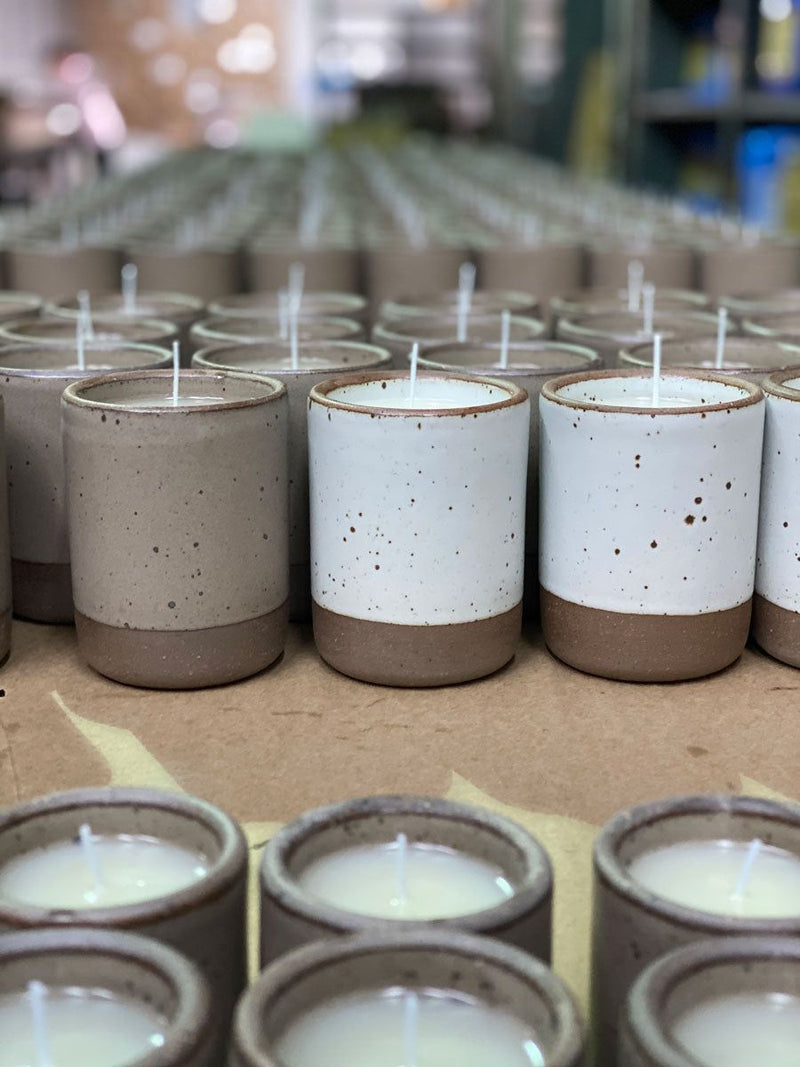 East Fork ceramic vessels with unglazed rims and bottoms and featuring iron speckles are lined up for candle production with wicks sticking out of each vessel