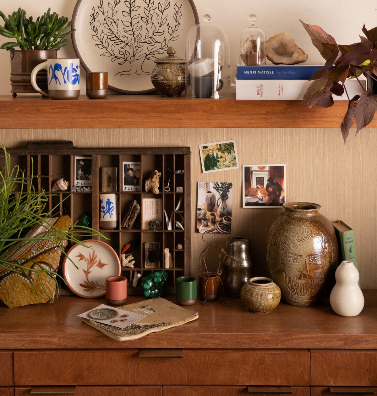 A collection of pottery, photos and small sculptural objects on a wooden surface.