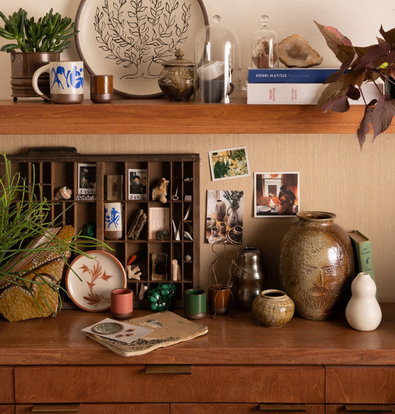 A collection of pottery, photos and small sculptural objects on a wooden surface.