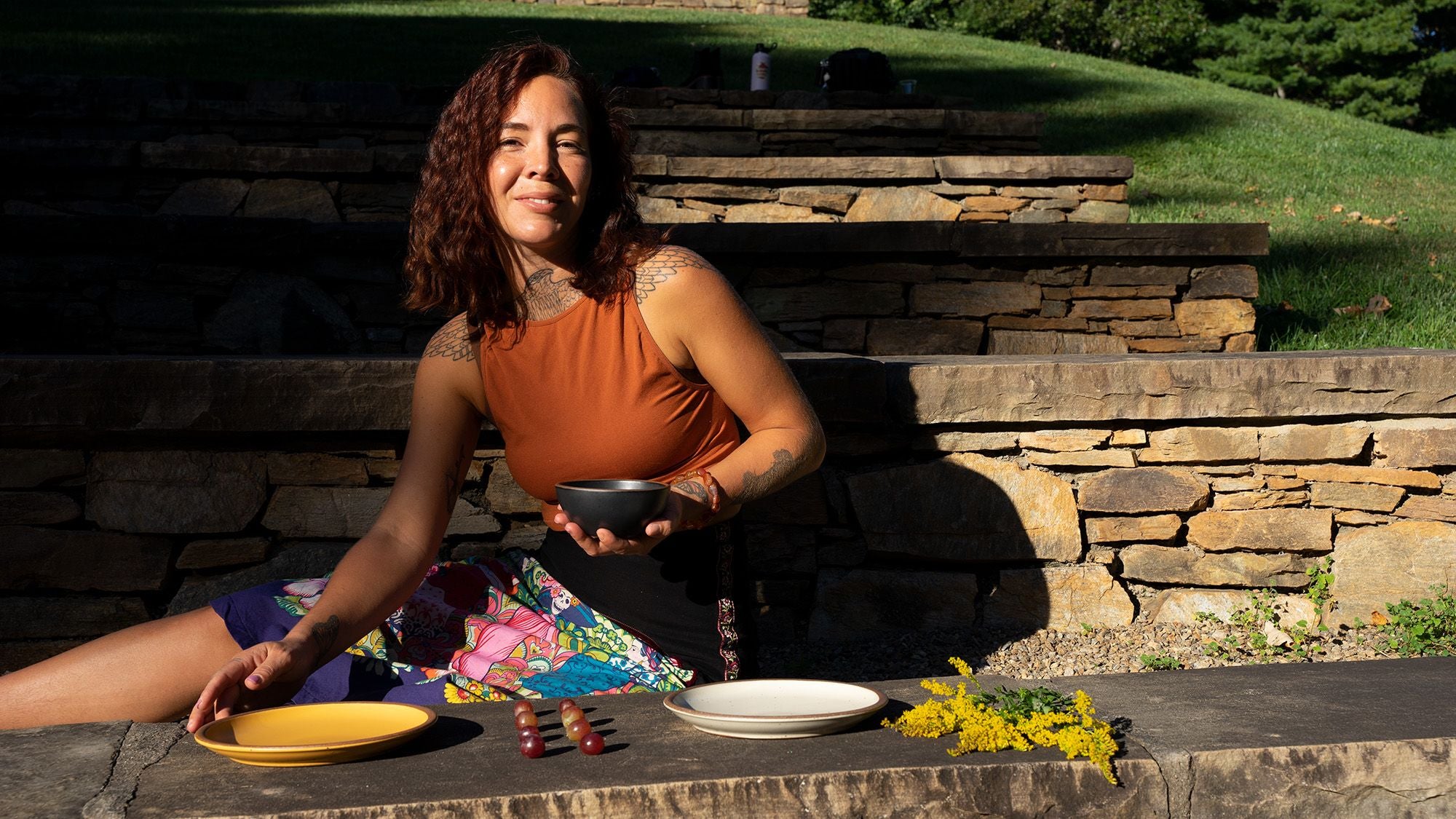 A person sits outside and is setting plates out on a long seat made of rocks