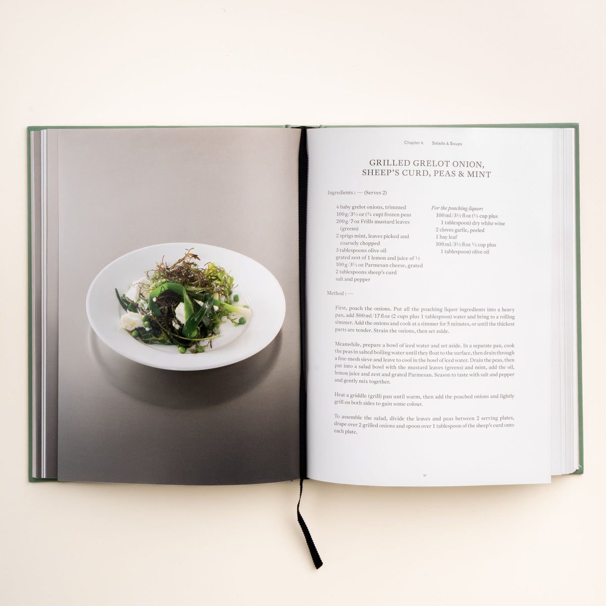 Open cookbook showing recipe for grilled grelot onion, sheep’s curd, peas, and mint with a plated salad on the left page.