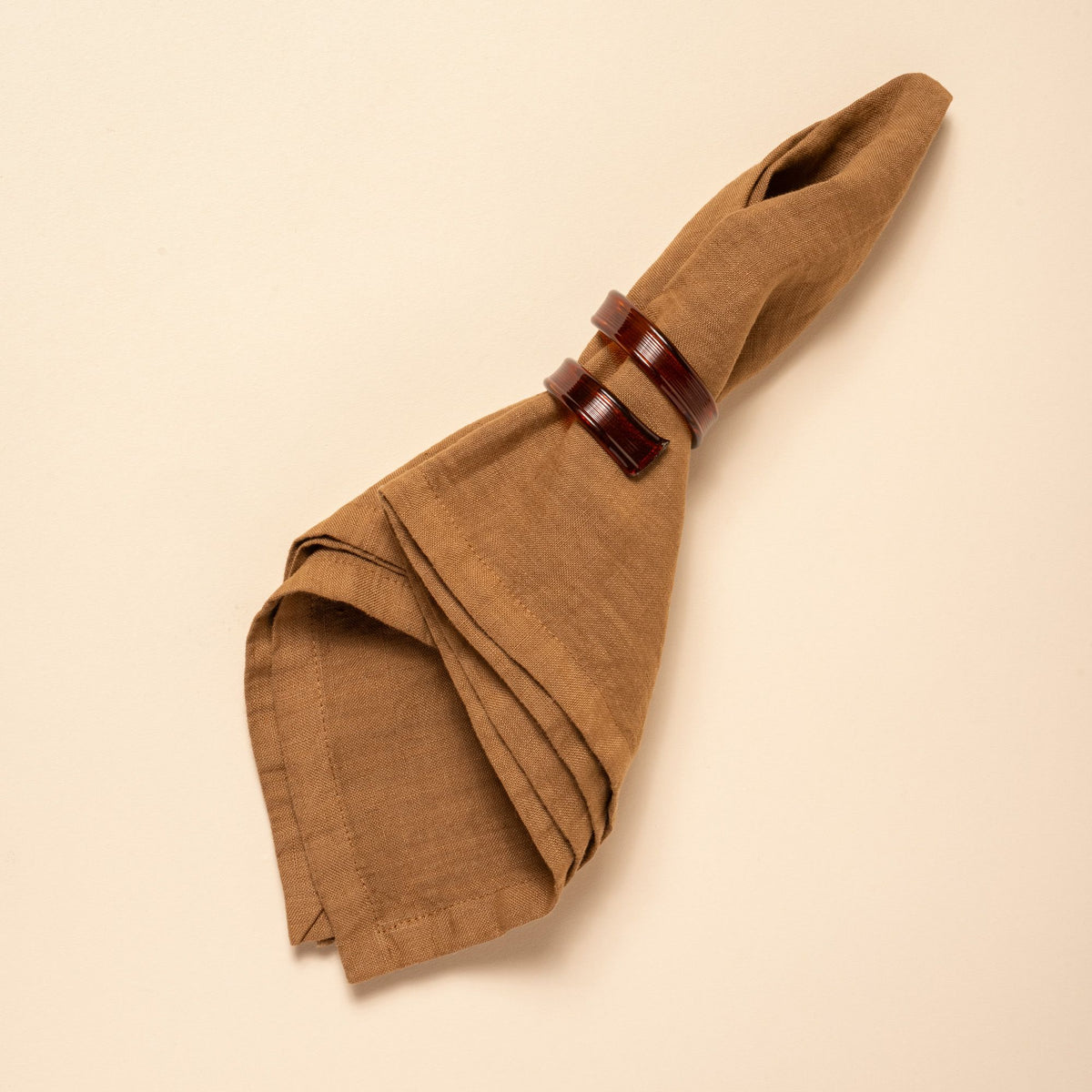 Brown linen napkin folded with curled recycle brown napkin rings, styled against a neutral background.