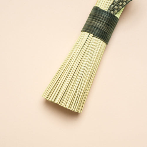 A closeup of a short scrub made out of broomcorn, tied together with cotton and a loop for hanging.