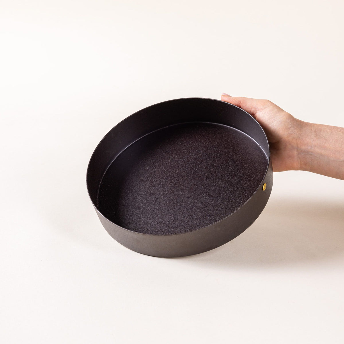 A hand holding a round black metal cake pan