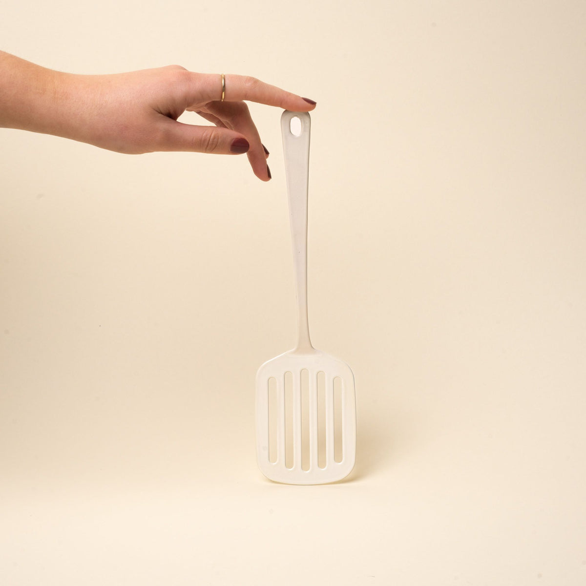 A hand props up a white enamel spatula with a hole at the end of the handle for hanging.