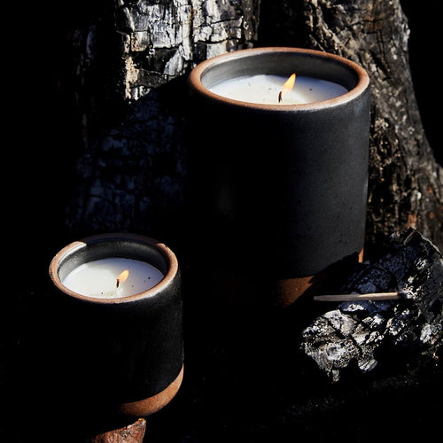 Large and small ceramic black candles lit in an earthy dark tree setting