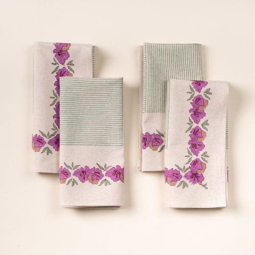 Four folded dinner napkins with green stripes and purple floral borders, arranged in two stacks on a cream background.