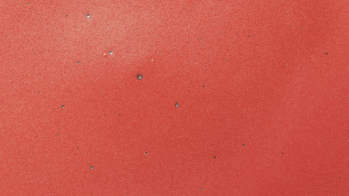 A closeup of a ceramic plate in a bold red color featuring iron speckles