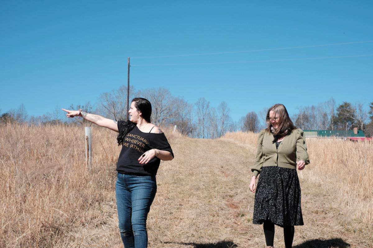 Two women walk outside, one of them points off into the distance