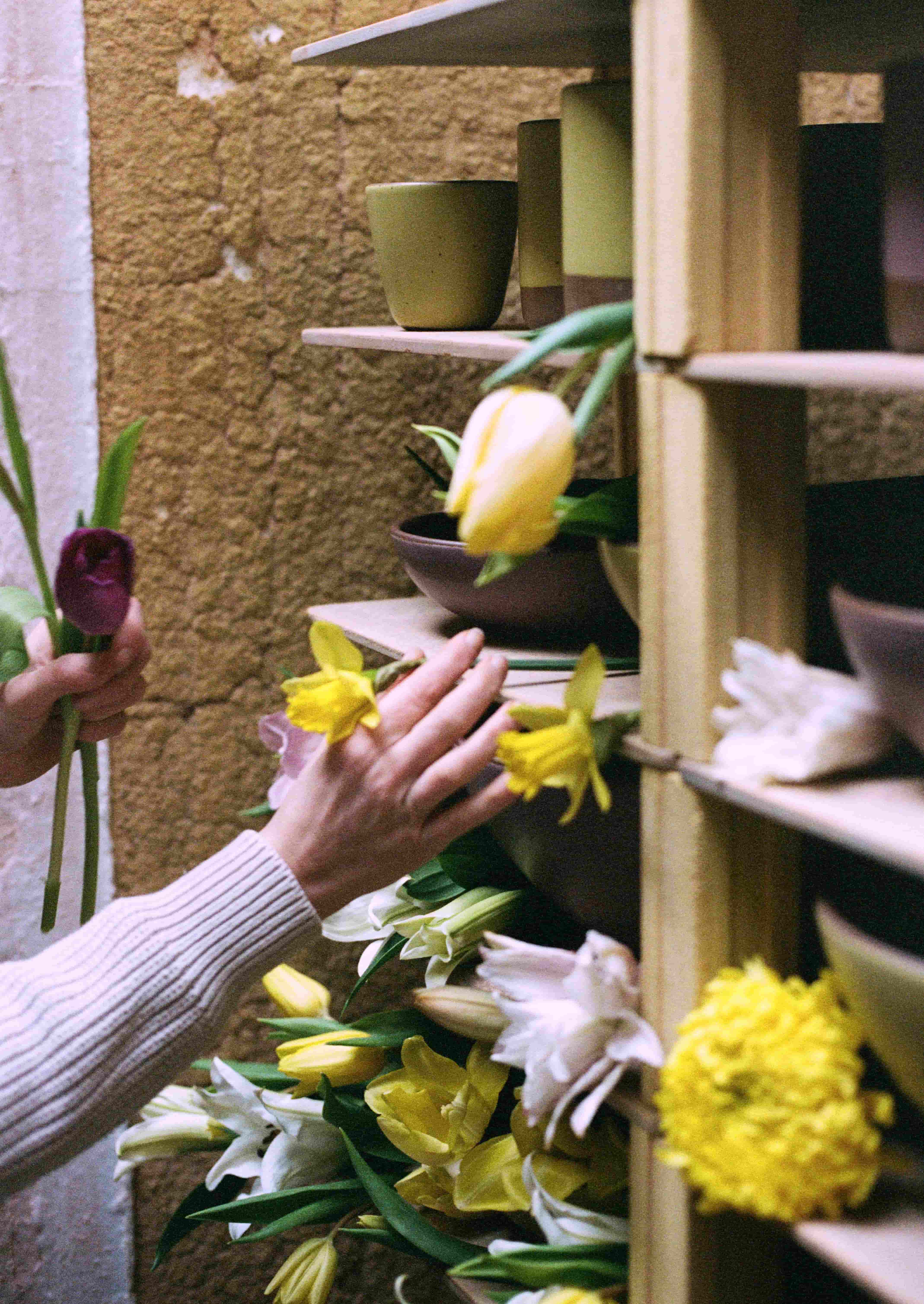 A hand reaching out to style flowers around pottery on a kiln cart.