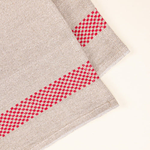 A closeup of a folded linen towel in a beige color with a red checkerboard stripe down the side