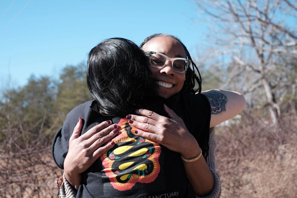 Two women hug outside with blue sky in the background
