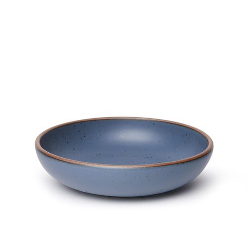 A large shallow serving ceramic bowl in a cool, medium blue color featuring iron speckles and an unglazed rim