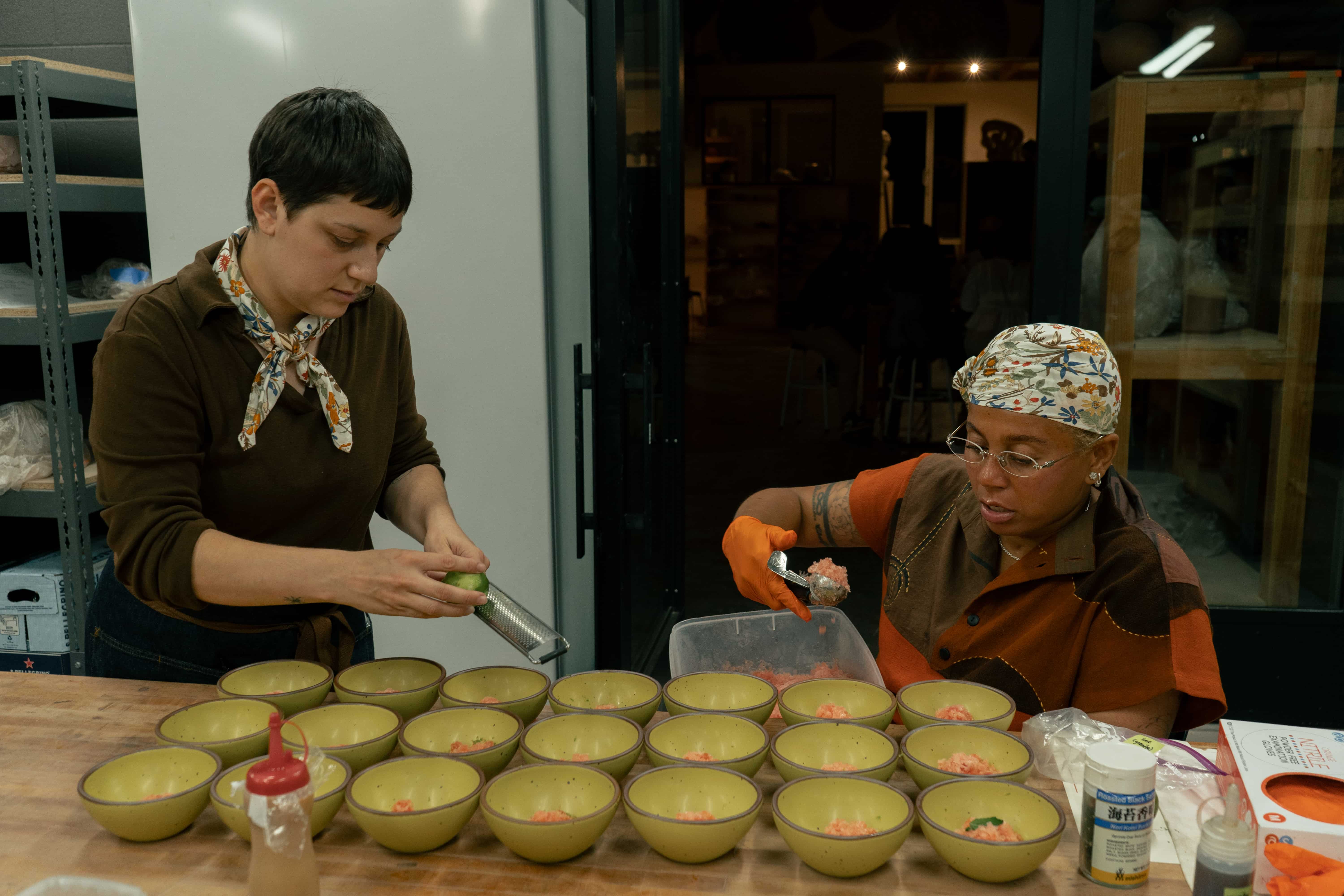 Lay and another person plating dishes on several ceramic bowls in a zesty yellow color.