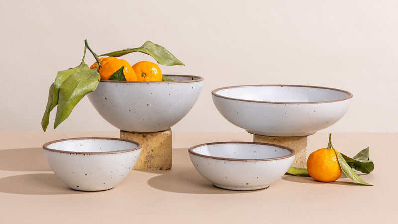 Set of ceramic bowls in a cool white color with fruits on a beige background