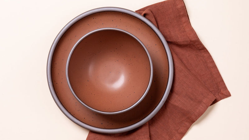 An overhead view of ceramic plates in cool terracotta with iron speckles, and a matching napkin