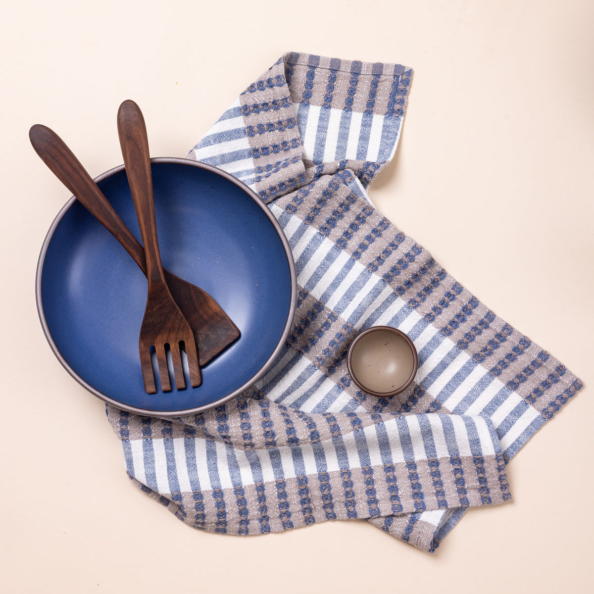 Blue ceramic bowl with wooden utensils on a blue and beige striped towel.