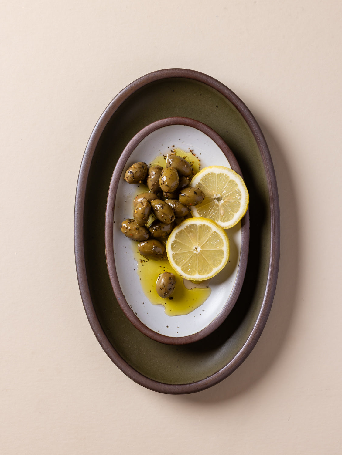Olive and white oval platters with lemon slices and olives on a beige background