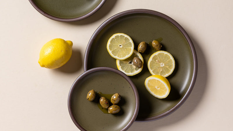 An overhead view of ceramic plates in an olive green color styled with lemons and olives.