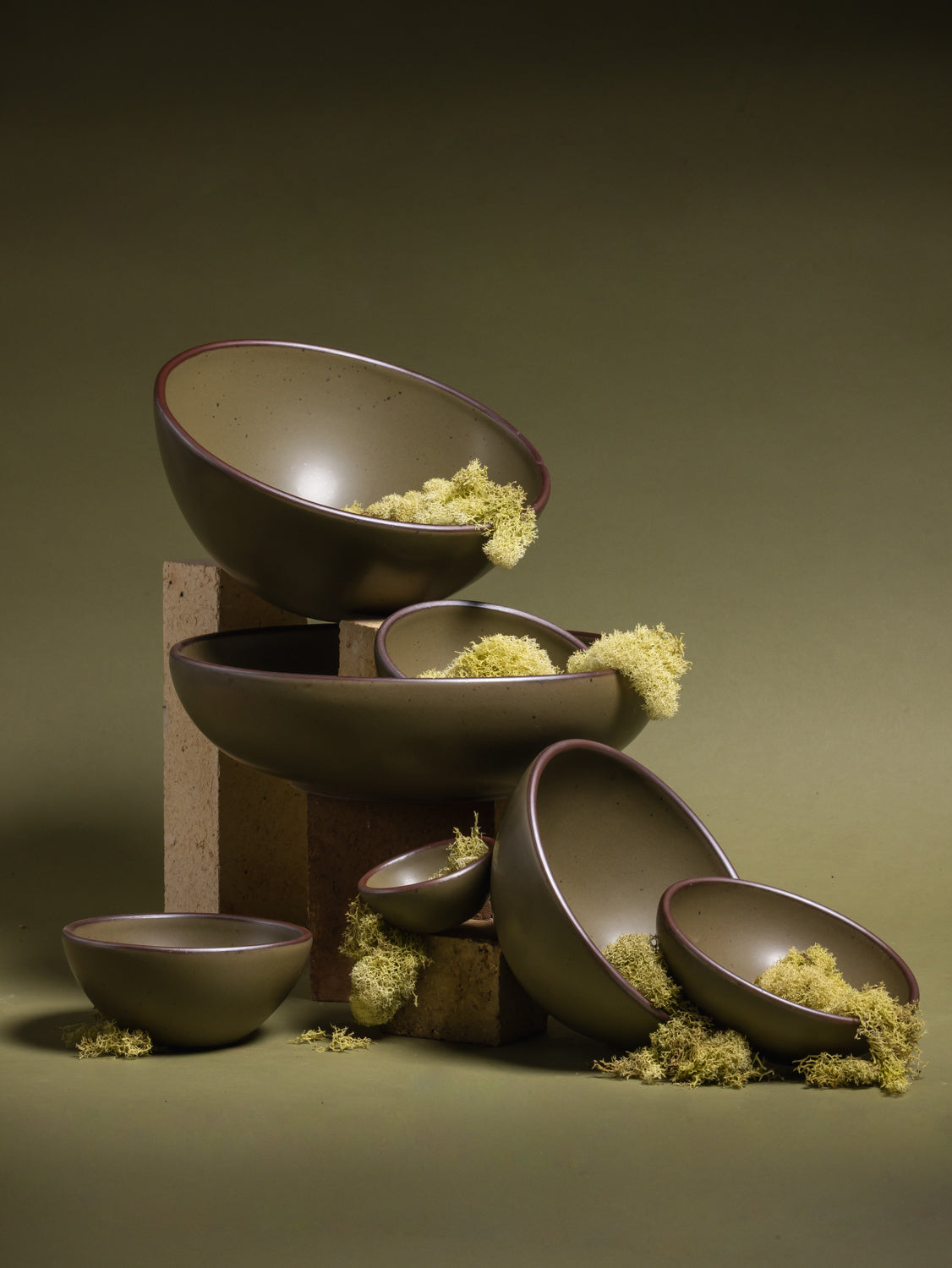 Stack of ceramic bowls in an olive green color with moss on a green background