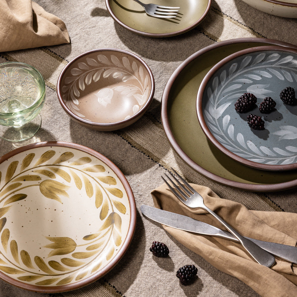 An overhead view of a table with hand painted dinnerware, silverware, napkin, and a coupe glass.