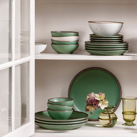 Set of green ceramic dinnerware on a white shelf with a neutral background