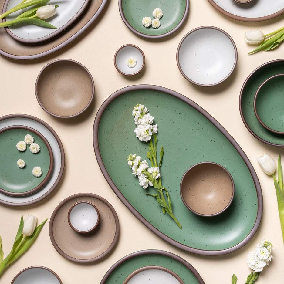 Collection of ceramic dishes in green and brown on a beige background with white flowers.