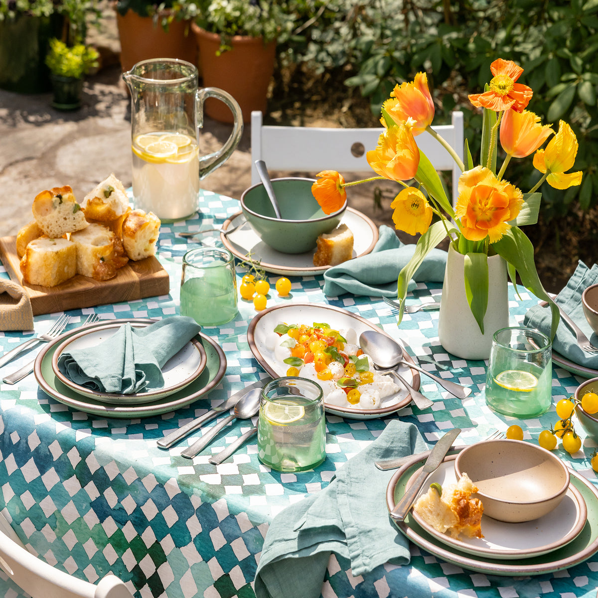 Outdoor table setting with a checkered tablecloth, plates, glasses, and a vase of yellow flowers.