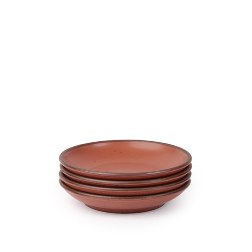 A stack of 4 small ceramic plates with a curved bowl edge in a cool terracotta color featuring iron speckles and an unglazed rim.