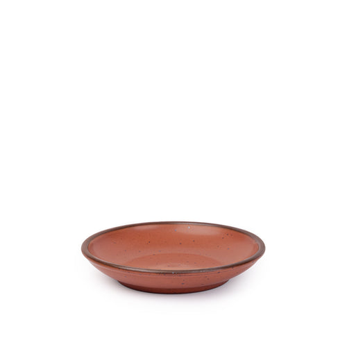 A small ceramic plate with a curved bowl edge in a cool burnt terracotta color featuring iron speckles and an unglazed rim.