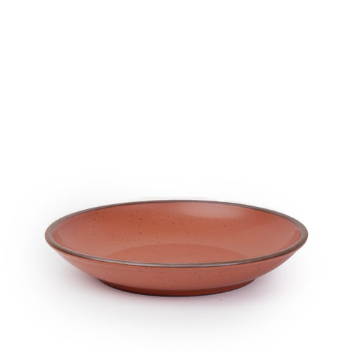 A large ceramic plate with a curved bowl edge in a cool burnt terracotta color featuring iron speckles and an unglazed rim.
