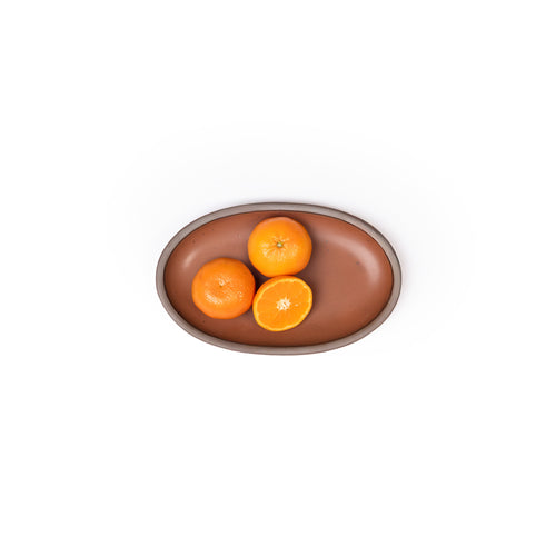 A small oval ceramic platter in a cool terracotta color featuring iron speckles and an unglazed rim, with small oranges