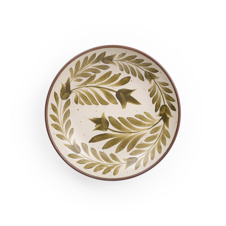 An overhead view of a large ceramic plate with a curved bowl edge in a warm, tan-toned, off-white color featuring iron speckles and an unglazed rim, with handpainted greenery in an olive green color.