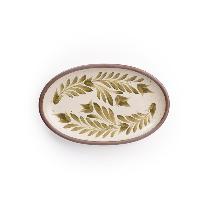 A medium oval ceramic platter in a warm, tan-toned, off-white color featuring iron speckles and an unglazed rim, with handpainted greenery in an olive green color.
