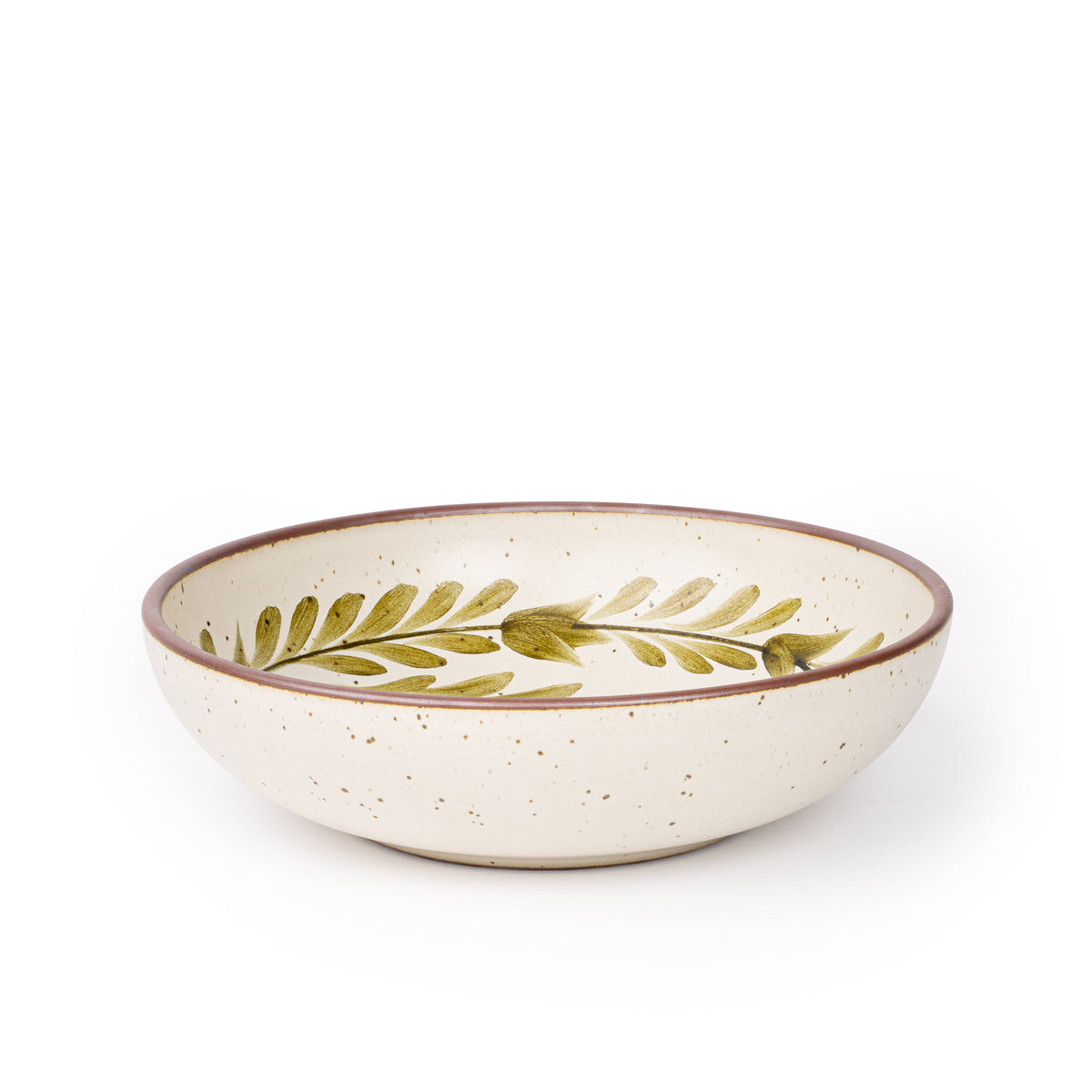 A large shallow serving ceramic bowl in a warm, tan-toned, off-white color featuring iron speckles and an unglazed rim, with handpainted greenery in an olive green color inside the bowl.