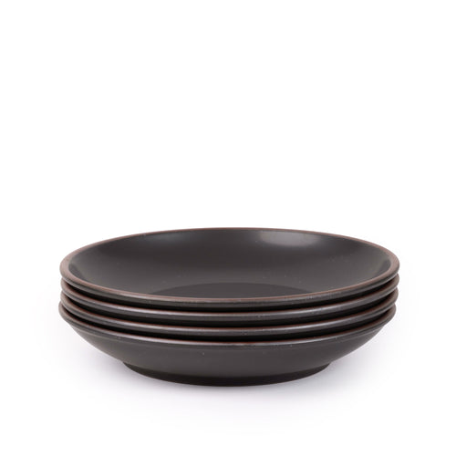 A stack of 4 large ceramic plates with a curved bowl edge in a graphite black color featuring iron speckles and an unglazed rim.