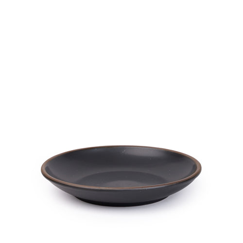 A medium ceramic plate with a curved bowl edge in a graphite black color featuring iron speckles and an unglazed rim.