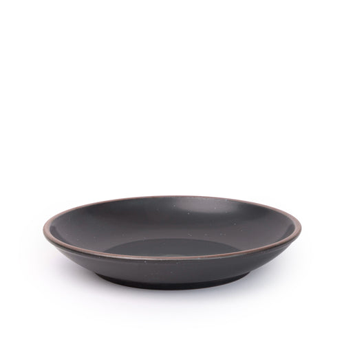 A large ceramic plate with a curved bowl edge in a graphite black color featuring iron speckles and an unglazed rim.