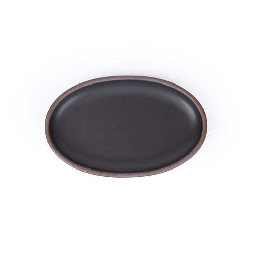A medium oval ceramic platter in a black color featuring iron speckles and an unglazed rim