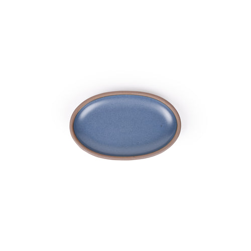 A small oval ceramic platter in a blue color featuring iron speckles and an unglazed rim