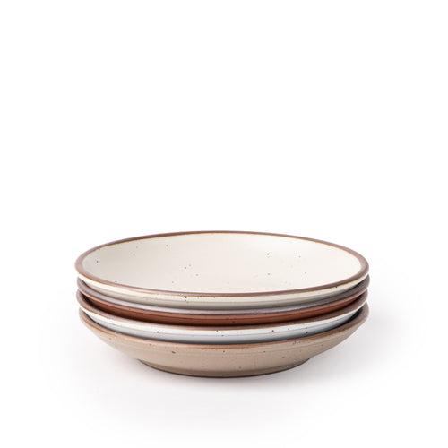 A stack of 4 medium ceramic plates with a curved bowl edge featuring iron speckles and an unglazed rim in warm off-white, cool terracotta, cool white, and pale warm brown colors.