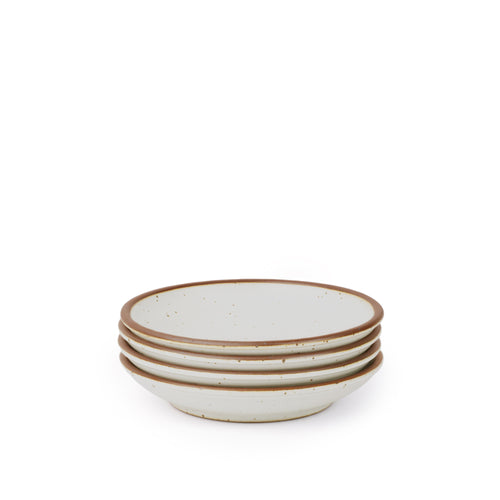 A stack of 4 small ceramic plates with a curved bowl edge in a cool white color featuring iron speckles and an unglazed rim.
