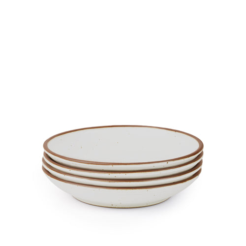 A stack of 4 medium ceramic plates with a curved bowl edge in a cool white color featuring iron speckles and an unglazed rim.